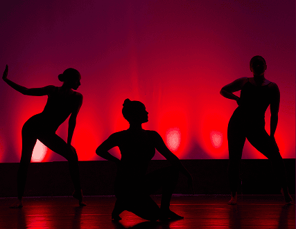 Photo of a silhouette of three dancers posing in front of a red curtain.