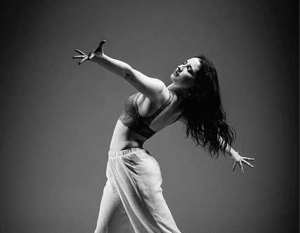 Black and white photo of a women performing modern dance on a dark background.