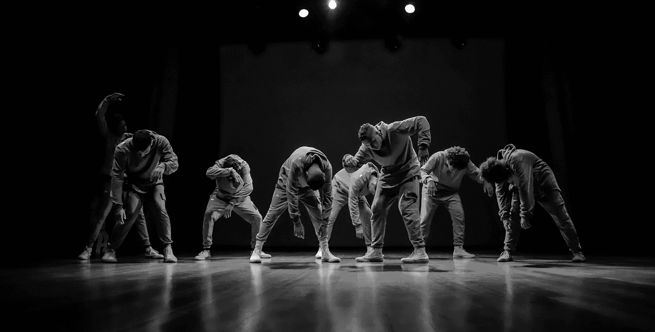 Black and white photo of a group of men performing modern dance on a stage.