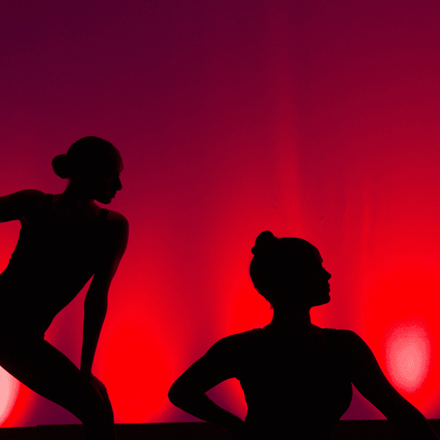 Photo of a silhouette of two dancers posing in front of a red curtain.