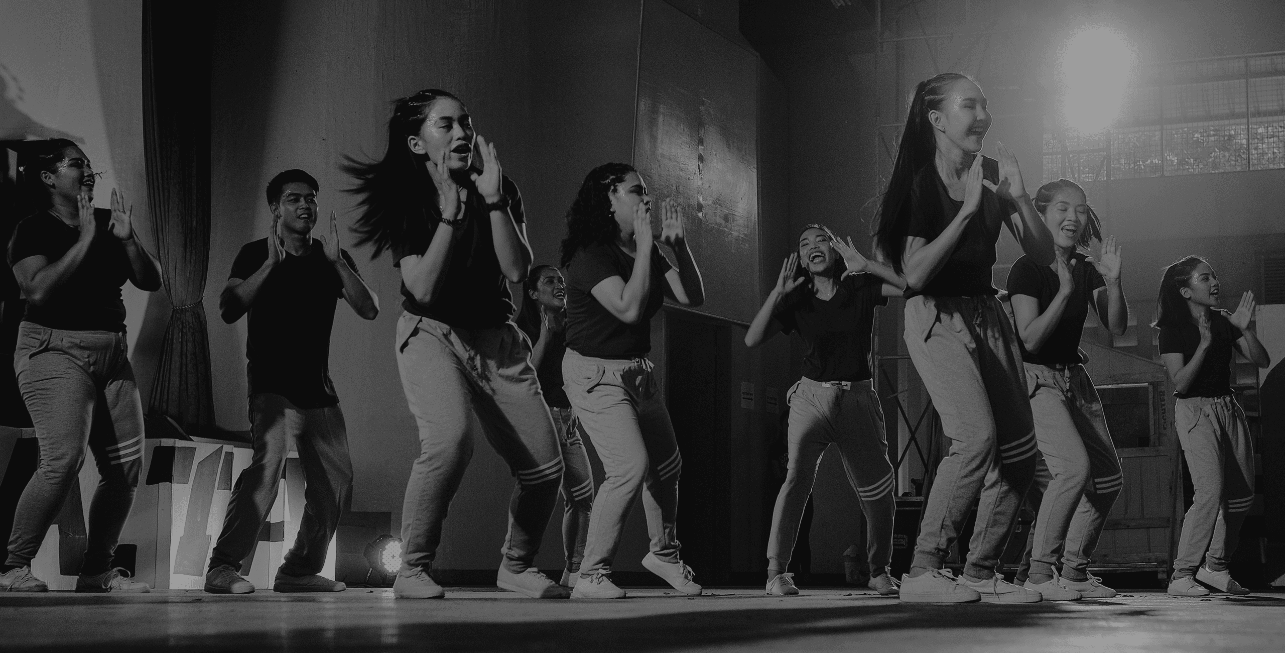 Black and white photo of teens rehearsing a dance routine on a stage.