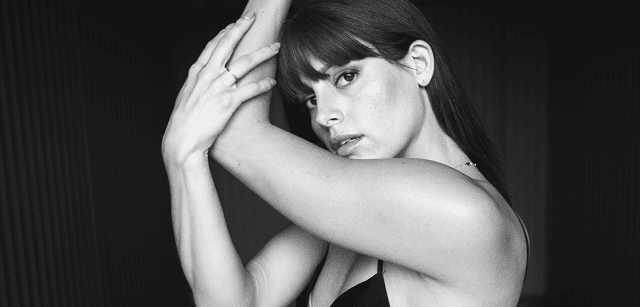Black and white portrait of a dance instructor posing in front of a dark background.