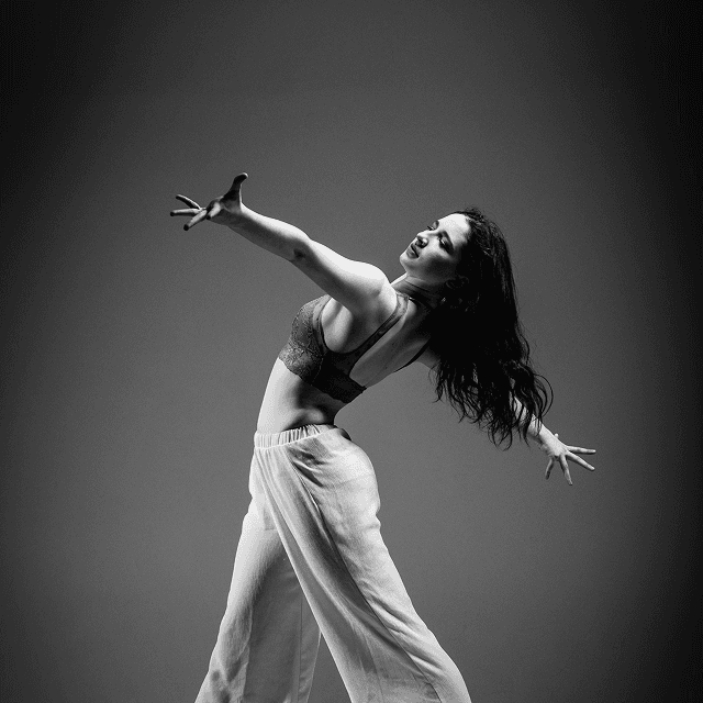 Black and white photo of a woman performing modern dance on a dark background.